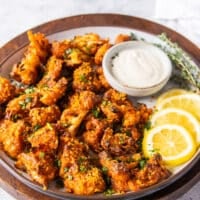 A plate of buffalo cauliflower with lemon slices and ranch bowl for dipping