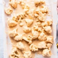 cauliflower tossed in batter and arranged on a baking sheet ready to bake