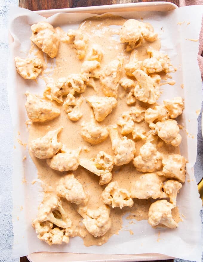 cauliflower tossed in batter and arranged on a baking sheet ready to bake 
