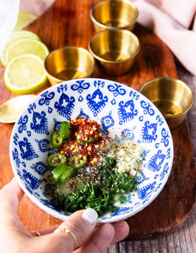 Ingredients for a drizzle sauce on the fried octopus including minced garlic, chili flakes, green chilies, lemon juice, olive oil, herbs
