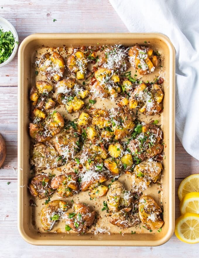 A tray of smashed potatoes finished with parmesan cheese, herbs, and more seasoning 