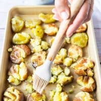 Oil and butter drizzled over a tray of smashed potatoes