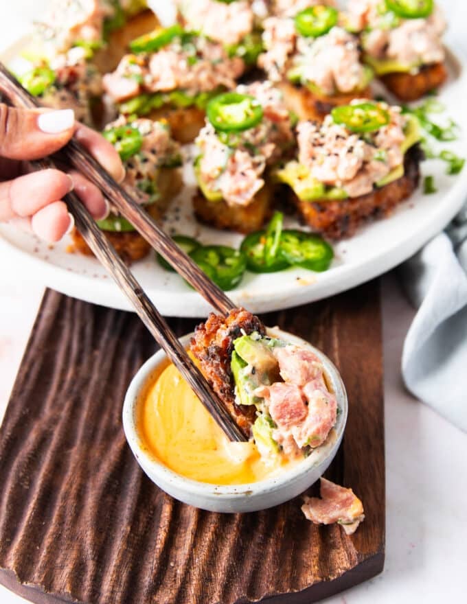 a hand dipping a spicy tuna crispy rice in spicy mayo using chopsticks