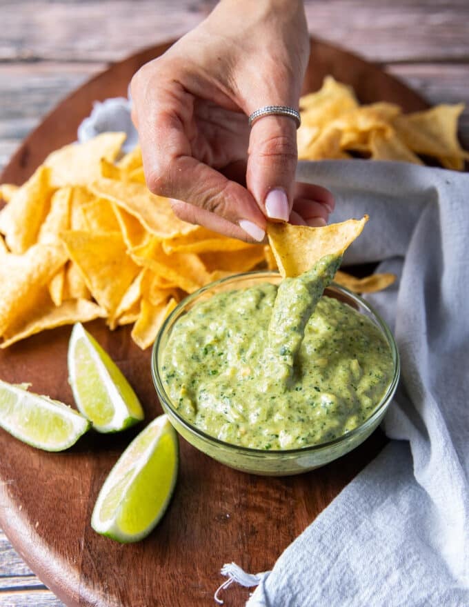 A hand scooping some poblano sauce with tortilla chips