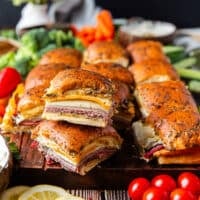close up of stacked roast beef sliders on a large board with bowls of creamy dips