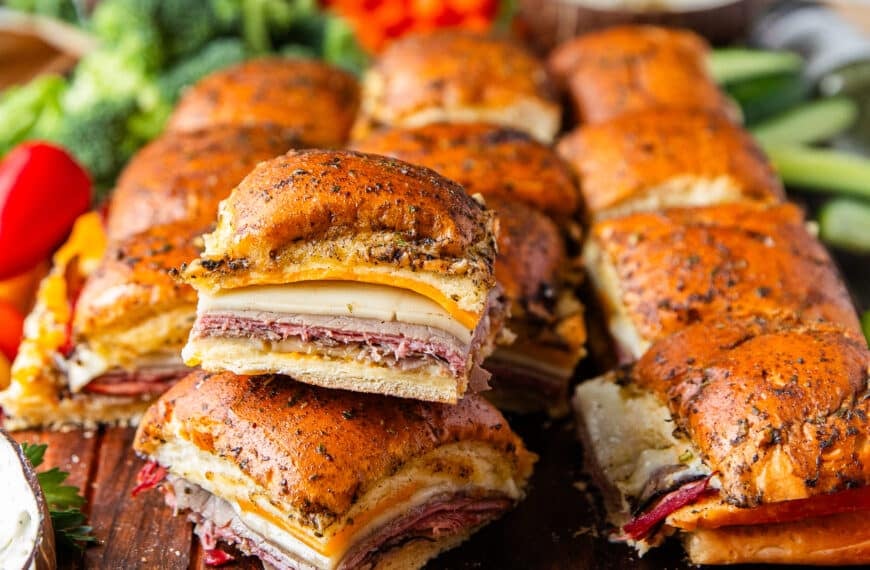 close up of stacked roast beef sliders on a large board with bowls of creamy dips