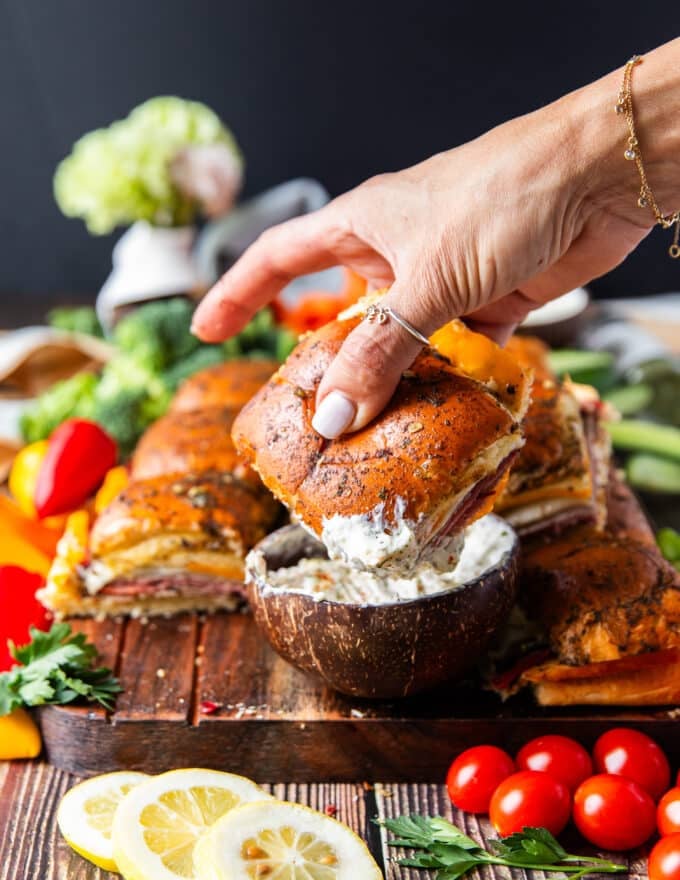 A hand dipping some roast beef sliders in a bowl of dip