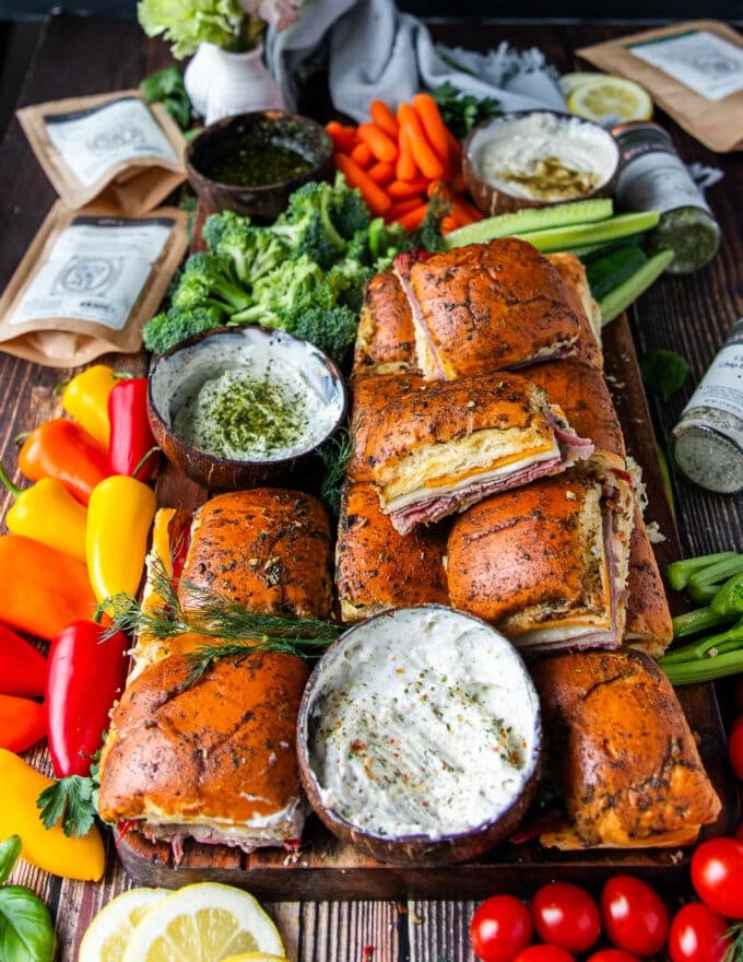 stacked roast beef sliders with a variety of dips on a cutting board along with some veggies