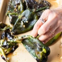A hand peeling off the skin from the charred peppers