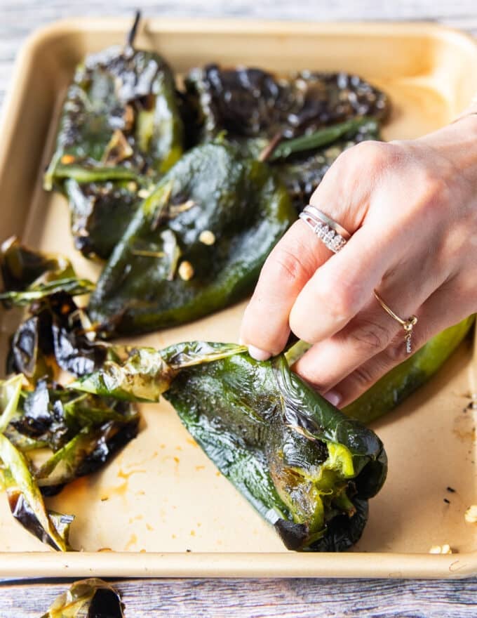 A hand peeling off the skin from the charred peppers