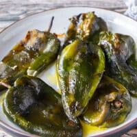 Side view of roasted poblanos on a plate with olive oil and salt