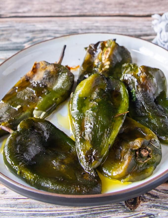 Side view of roasted poblanos on a plate with olive oil and salt