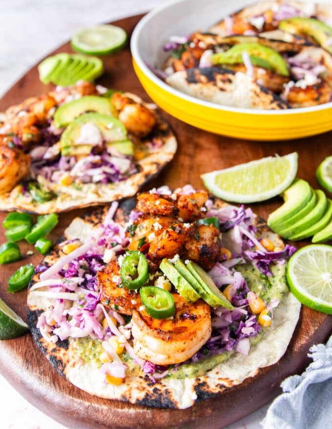 shrimp tacos on a board fully assembled with lime wedges on the side and ready to serve