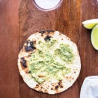 charred tortilla with a spread of poblano sauce and taco sauce