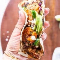 A hand holding a shrimp taco close up full assembled and ready to eat