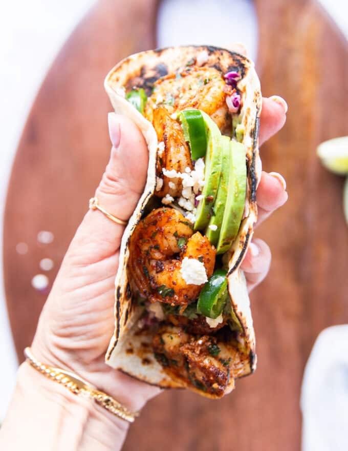 A hand holding a shrimp taco close up full assembled and ready to eat