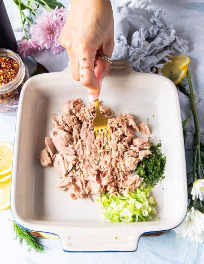 A hand mashing the canned tuna into a bowl to make the texture smooth