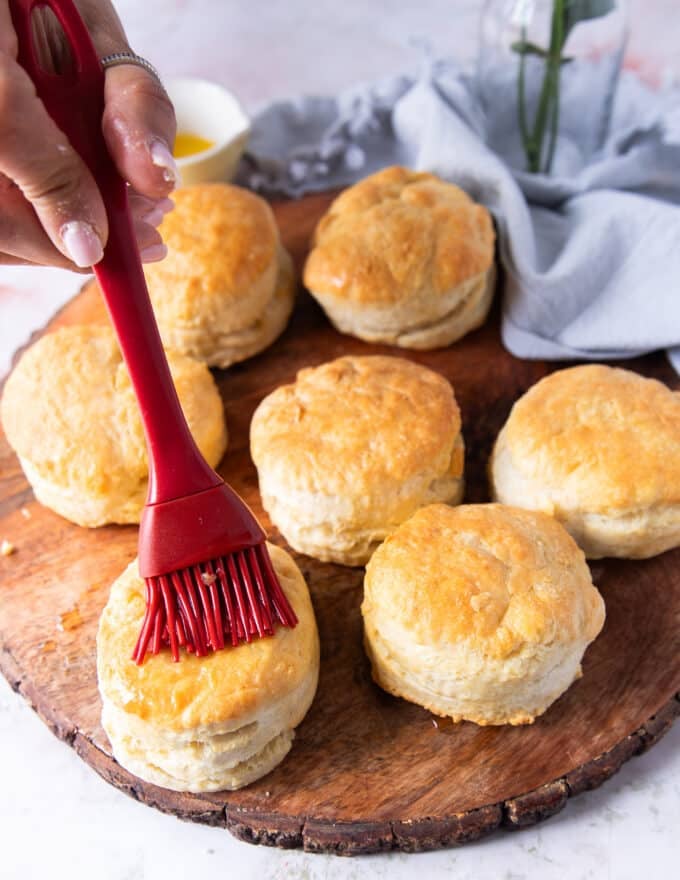 A brush brushing melted butter over the warm biscuits right out of the air fryer