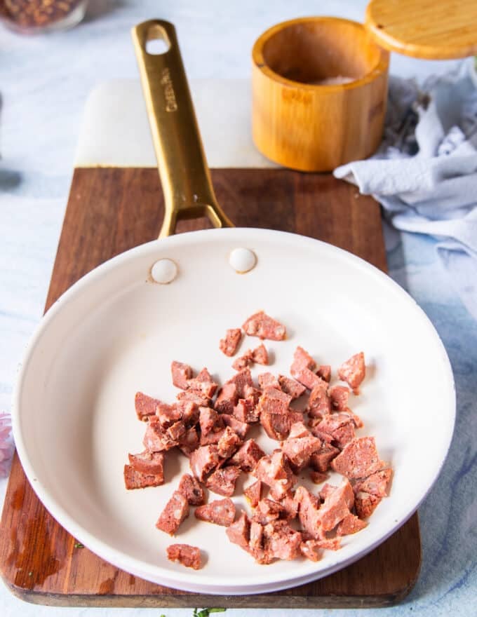 The bacon or sausage added to a skillet over high heat and ready to crisp up