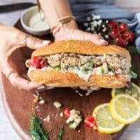 two hands holding a finished sardine sandwich fully assembled and ready to enjoy showing the layers