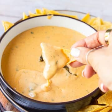 A hand holding a chip dipping the chips in the smoked queso