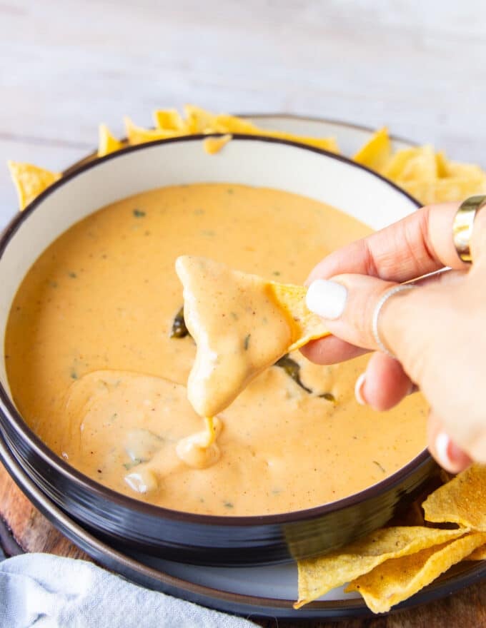 A hand holding a chip dipping the chips in the smoked queso 
