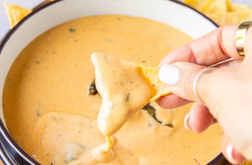 A hand holding a chip dipping the chips in the smoked queso