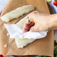 A hand patting the cod fish dry using paper towels
