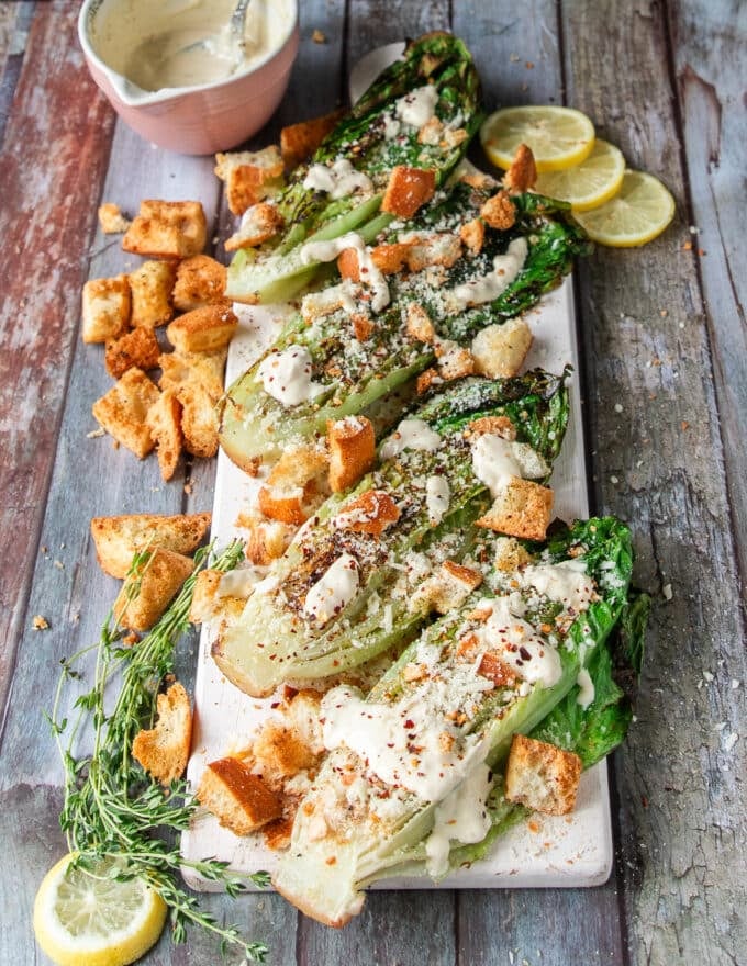 A white board white grilled romaine salad topped with parmesan cheese and some croutons showing the charred romaine and creamy dressing