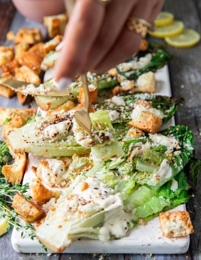 A fork taking a bite of the grilled romaine salad showing the crips centers of the romaine lettuce contrasting the charred exterior