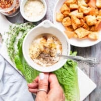A hand holding a bowl with the salad dressing ingredients ready to be whisked and blended.