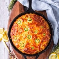 Top view of a jalapeno cornbread baked in a cast iron skillet with jalapeno slices on top and cheddar cheese