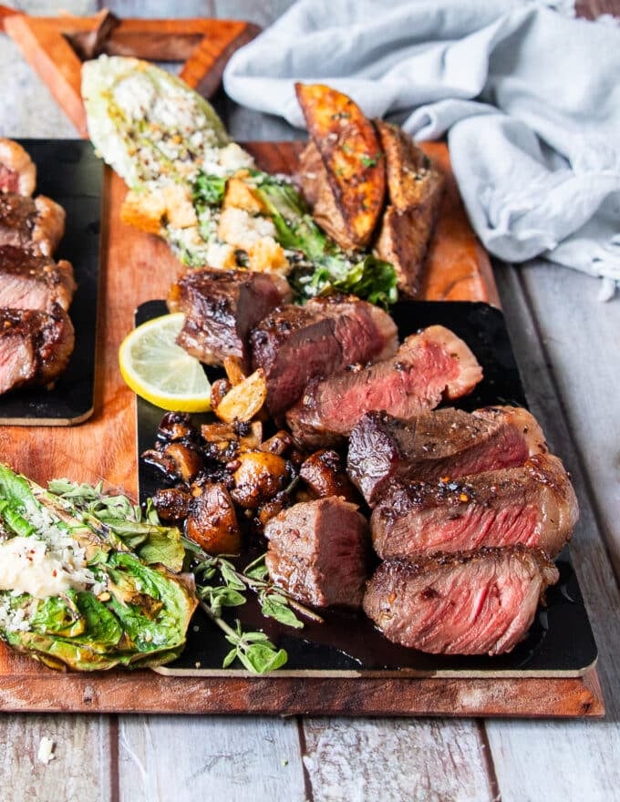A full plate of pincanha steaks served with potato wedges and grilled romaine salad with the meat sliced perfectly to show how perfect done