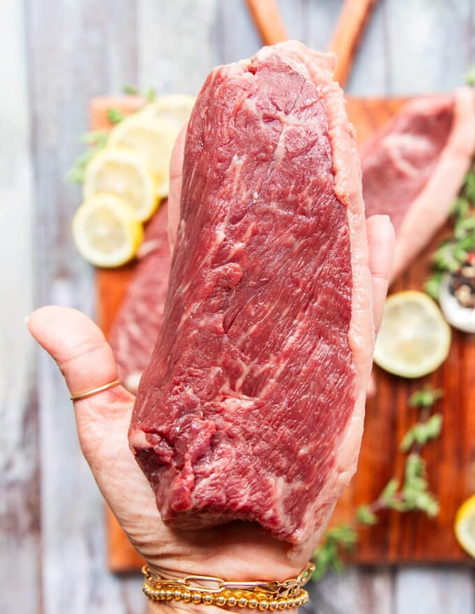 A hand holding a piece of picanha steak close up showing the fat slab clearly and showing what to look like when buying the meat 