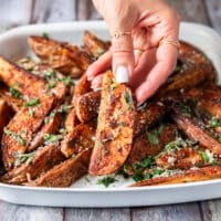 A hand holding a potato wedge close up showing how crispy the outside is and showing off the bold seasoning