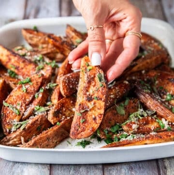 A hand holding a potato wedge close up showing how crispy the outside is and showing off the bold seasoning