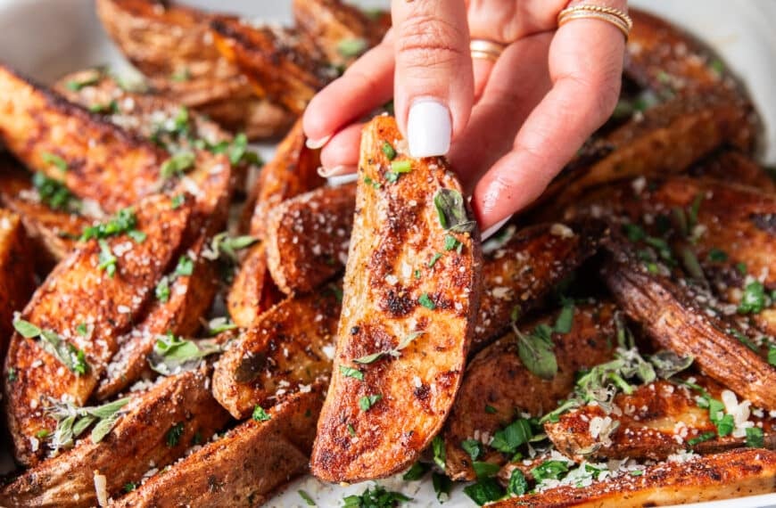 A hand holding a potato wedge close up showing how crispy the outside is and showing off the bold seasoning