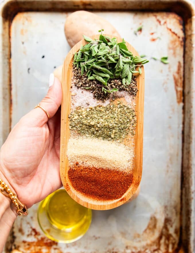 A hand holding a large plate with different seasonings for the potato wedge seasoning and some herbs