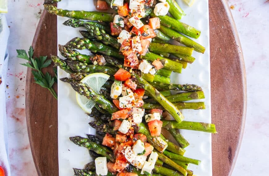 A plate with baked asparagus topped with fresh tomatoes and feta mixture for a light side dish.