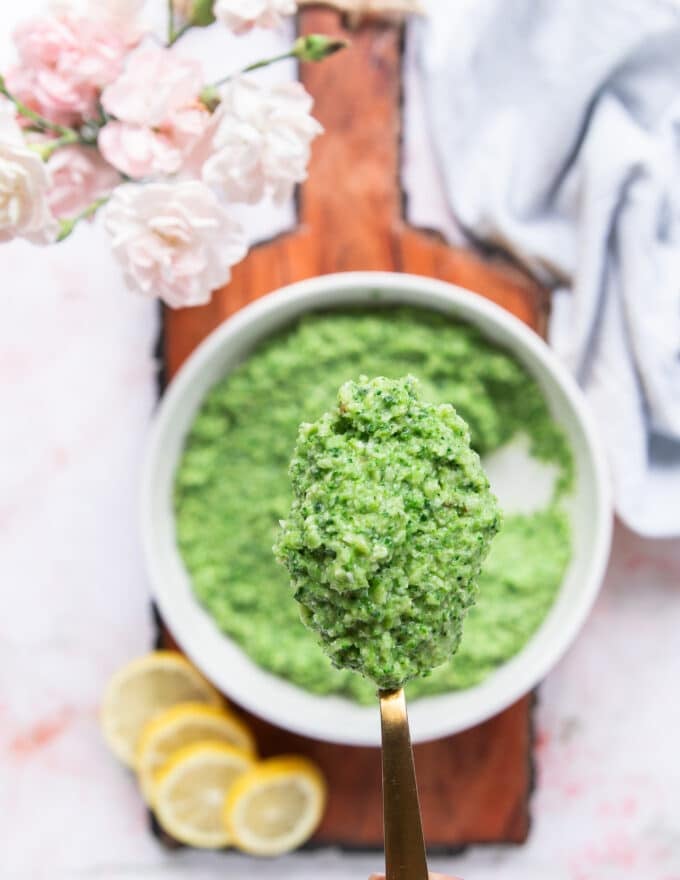 A spoon holding a close up of broccoli pesto