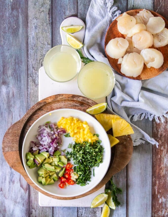 Ingredients to make scallop ceviche including fresh raw, tender scallops, the citruses juiced, finely diced onions, cilantro, chilies, avocados and pineapple
