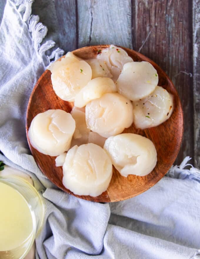 A hand holding a plate of cleaned scallops, patting dry