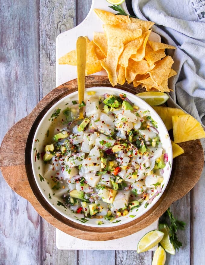A full plate of scallop ceviche surrounded by tortilla chips and lime wedges