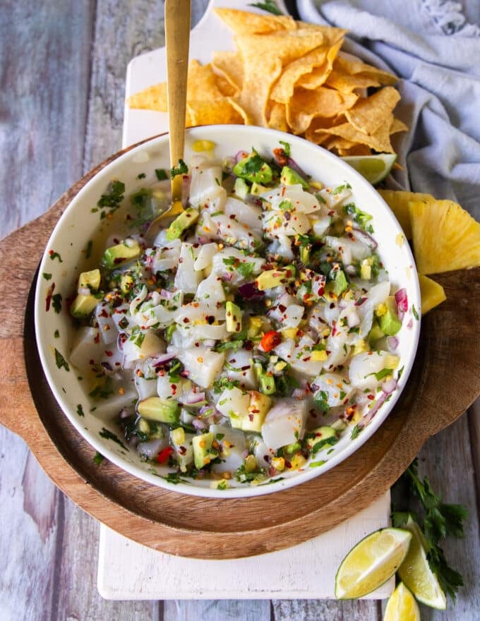 A bowl of scallop ceviche with cut scallops mixed with citrus, onions, chilies, cilantro, and a spoon used to serve it