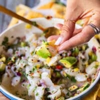 A hand holding a piece of tortilla scooping scallop ceviche