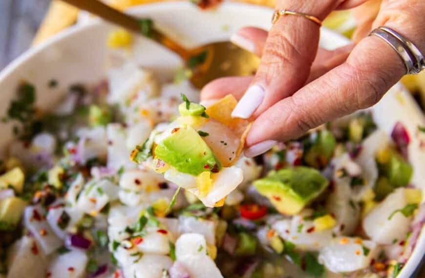 A hand holding a piece of tortilla scooping scallop ceviche