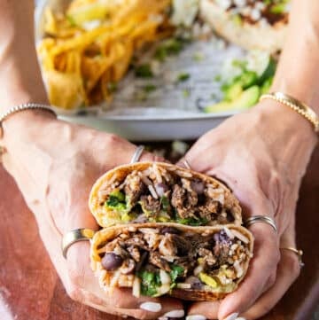 A birria Burrito cut in half and a hand holding to show the juicy beef birria meat, cilantro and onions