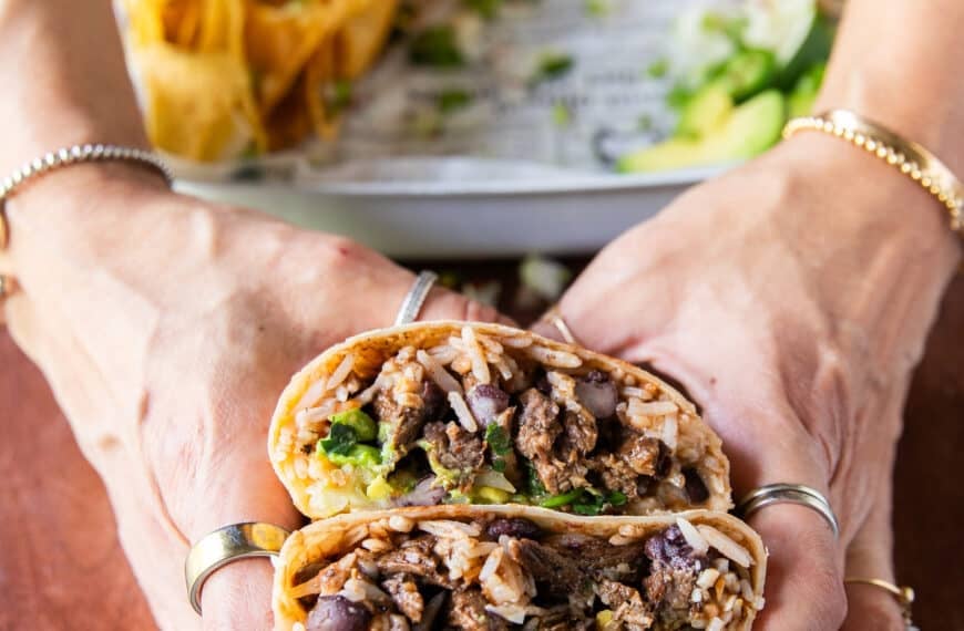A birria Burrito cut in half and a hand holding to show the juicy beef birria meat, cilantro and onions