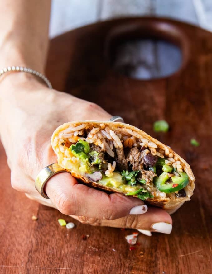 A hand holding half a burrito to be dipped in consommé 