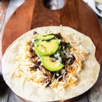 The birria meat and consommé is added, minced onions and cilantro and optional avocado too